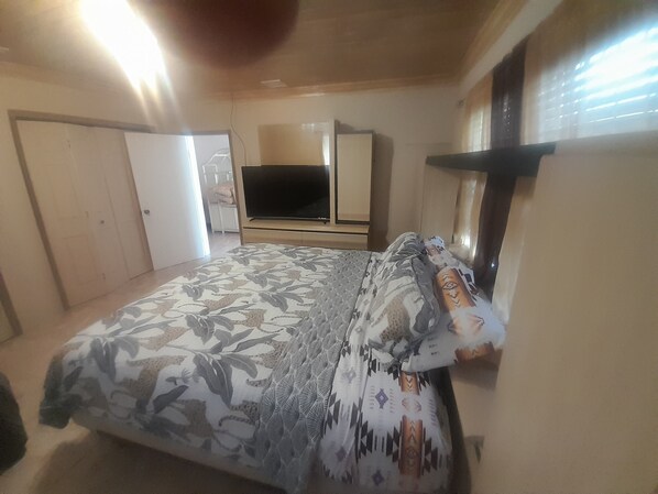 A bedroom with a bed, a TV, a wardrobe, and a window.