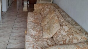 Ein Wohnzimmer mit einem gemusterten Sofa, einem Holzesstisch und einer Küchenzeile im Hintergrund.