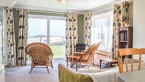 A room with a view of the sea, wicker furniture, a bookshelf, and a table. - Apartment 1 Waterrs Edge (Newquay)