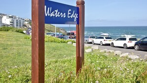 A sign reading 'Waters Edge' with a coastal view and parked cars. - Apartment 1 Waterrs Edge (Newquay)