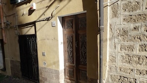 A building with a stone facade, a wooden door with intricate carvings, and a metal gate. - Loft in the old Town (Alghero)