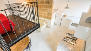 A modern kitchen with a gas stove, white cabinets, and a stone wall. - Loft in the old Town (Alghero)