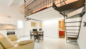 A spacious living area with a high ceiling, a dining table with chairs, a sofa, and a staircase with a metal railing. - Loft in the old Town (Alghero)