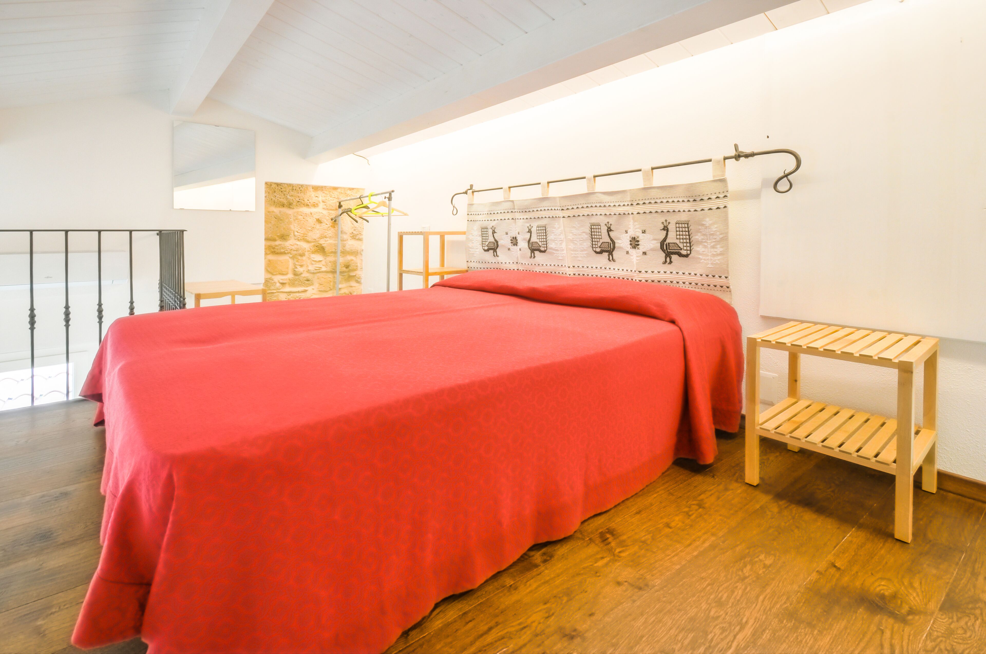 A spacious bedroom with a large bed, wooden flooring, a stone accent wall, and a simple wooden bench.