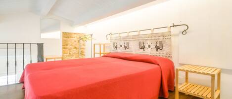 A spacious bedroom with a large bed, wooden flooring, a stone accent wall, and a simple wooden bench.