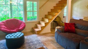 Una habitación con una escalera de madera, una silla roja, un sofá marrón y un tapete estampado.