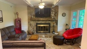 Una sala de estar con chimenea, un sofá, un sillón rojo y un televisor.