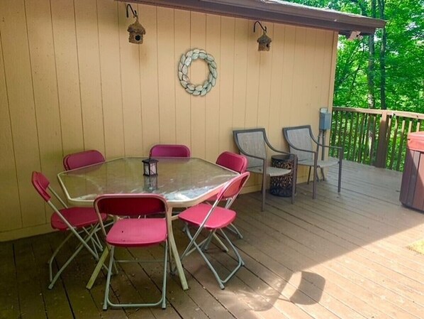 A covered patio with a glass table surrounded by red chairs, a wooden deck, and a railing.