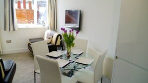 Comedor con mesa de vidrio, sillas blancas y un jarrón de flores moradas.