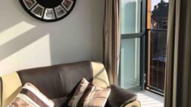 Un salón con sofá de cuero, un reloj de pared y un ventanal con cortinas.