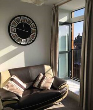 Een woonkamer met een leren bank, een wandklok en een groot raam met gordijnen.