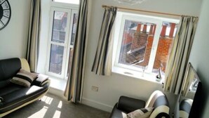 Una sala de estar con un sofá, una silla, una ventana con cortinas y vistas a un edificio de ladrillo.