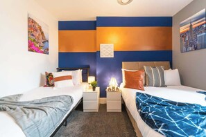 A hotel room with two beds, a nightstand with a lamp, and a wall with a cityscape painting. - Jesouth Exquisite Suite Dazzling Chic Centre (Kingston upon Hull)