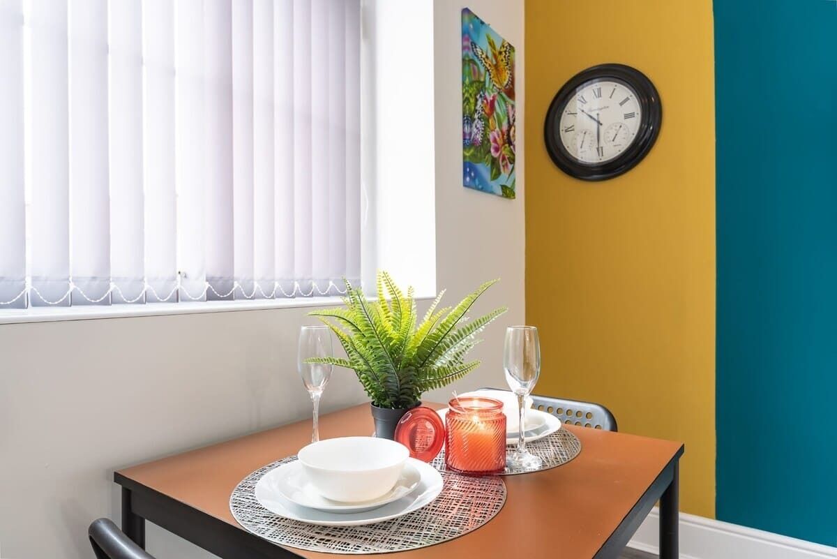 A dining table with a plant, two wine glasses, a candle, and a clock on the wall.