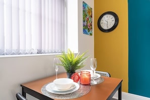 A dining table with a plant, two wine glasses, a candle, and a clock on the wall. - Jesouth Exquisite Suite Dazzling Chic Centre (Kingston upon Hull)