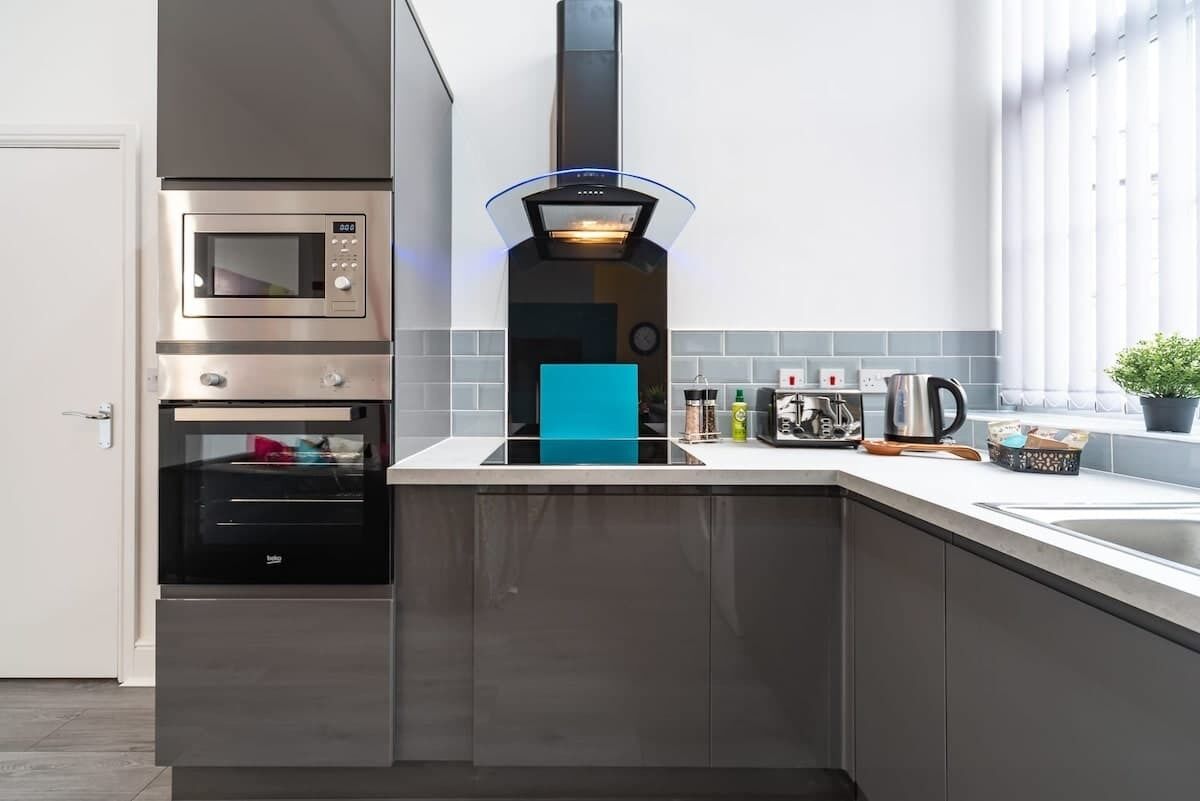 A modern kitchen with a built-in oven, a range hood, and a countertop with various kitchen items.
