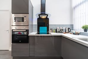 A modern kitchen with a built-in oven, a range hood, and a countertop with various kitchen items. - Jesouth Exquisite Suite Dazzling Chic Centre (Kingston upon Hull)