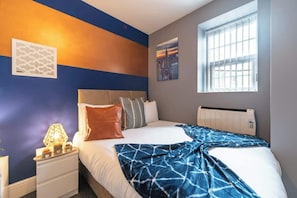 A hotel room with a bed, bedside table, lamp, and a window with blinds. - Jesouth Exquisite Suite Dazzling Chic Centre (Kingston upon Hull)