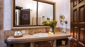 A bathroom with a large mirror, a sink, a towel rack, and a small shelf with toiletries. - Beautiful view of the arch, Club Cascadas suite with kitchen. (Cabo San Lucas)