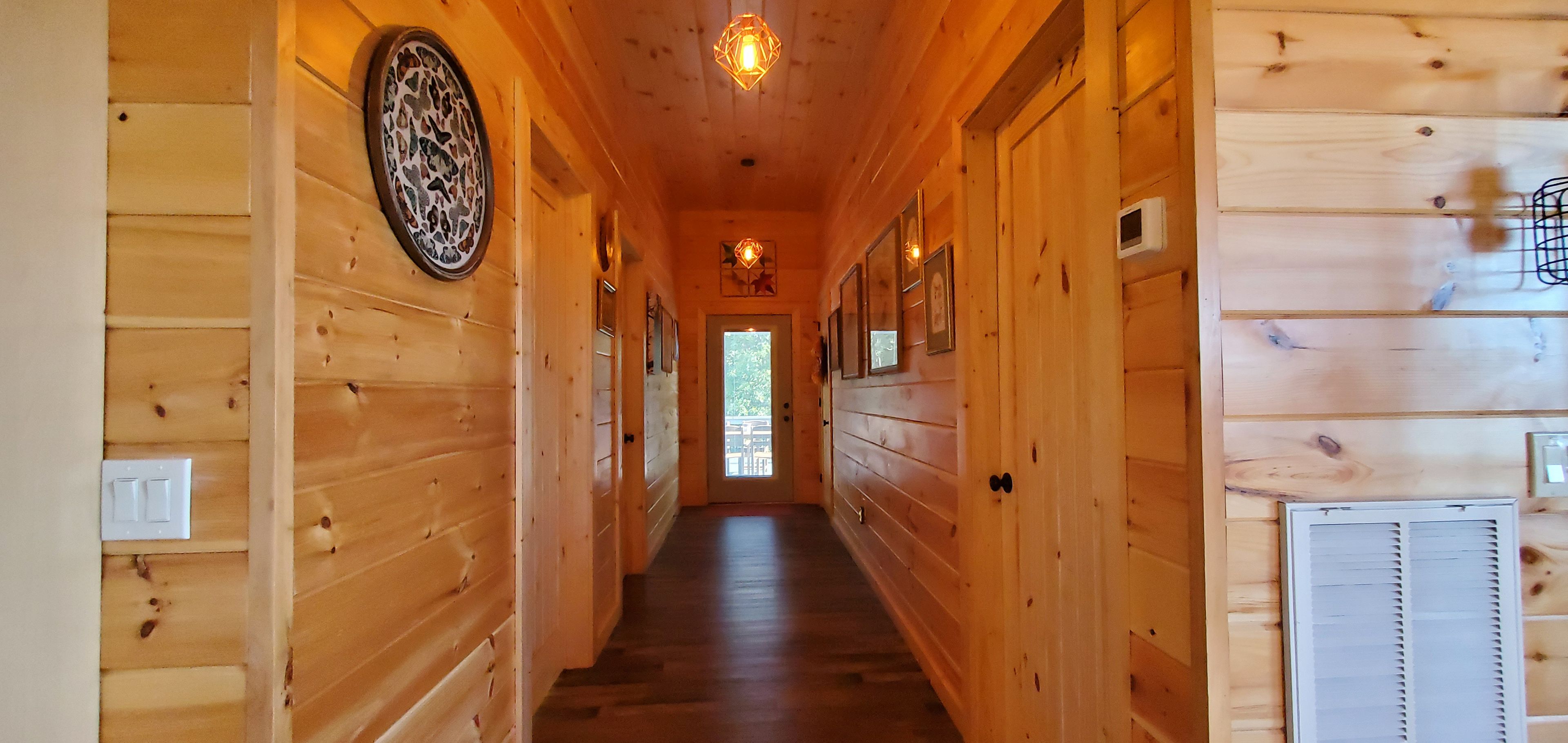 Un couloir en bois, avec une porte au fond, un luminaire au plafond et un autre fixé au mur.