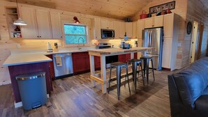 Una cucina compatta con mobili in legno, un frigorifero in acciaio inossidabile, un forno a microonde e un lavello. C'è un piccolo angolo bar con sgabelli e una finestra sopra il lavello.