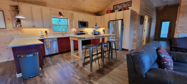 A compact kitchen with wooden cabinets, a stainless steel refrigerator, a microwave, and a sink. There is a small bar area with stools and a window above the sink. - The Barn at Frog Hollow, Delano.  Rare find with 5 bedrooms, sleeps up to 15! (Delano)
