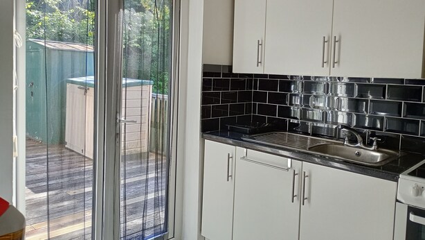 A kitchen with white cabinets, a black tiled backsplash, and a stainless steel sink. - Kingfisher Cottage Caernarfon-river rambling & relaxing, in a beautiful setting  (Caernarfon)