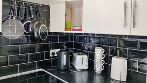 A kitchen with black tiled backsplash, white cabinets, a kettle, a toaster, a coffee maker, and hanging pots. - Kingfisher Cottage Caernarfon-river rambling & relaxing, in a beautiful setting  (Caernarfon)