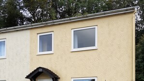 A two-story building with a beige textured exterior, a white door with a small porch, and a bench outside. - Kingfisher Cottage Caernarfon-river rambling & relaxing, in a beautiful setting  (Caernarfon)
