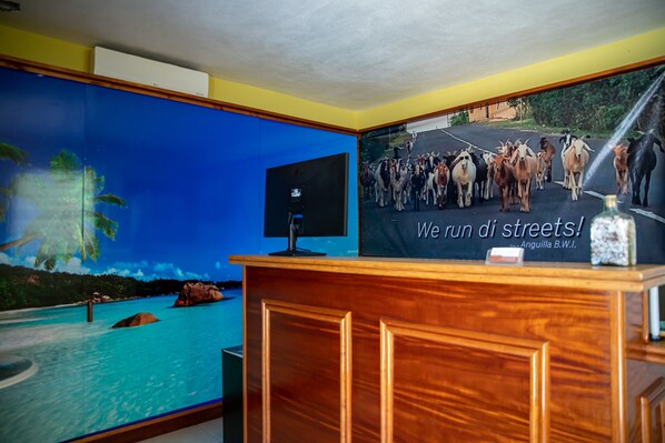 A reception desk with a television screen, a poster of a road with goats, and a pool with rocks. - Easy Corner Villas (South Hill)