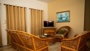 A living room with wicker furniture, a flat-screen TV, and a painting on the wall.