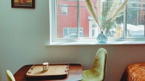 A room with a window overlooking a street, a chair, a small table with a tray, and a vase with pampas grass. - CoralXscape: curated 2 bedroom in Philly near everything! (Philadelphia)