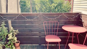 A wooden deck with a metal chair and a small table, surrounded by potted plants. - CoralXscape: curated 2 bedroom in Philly near everything! (Philadelphia)