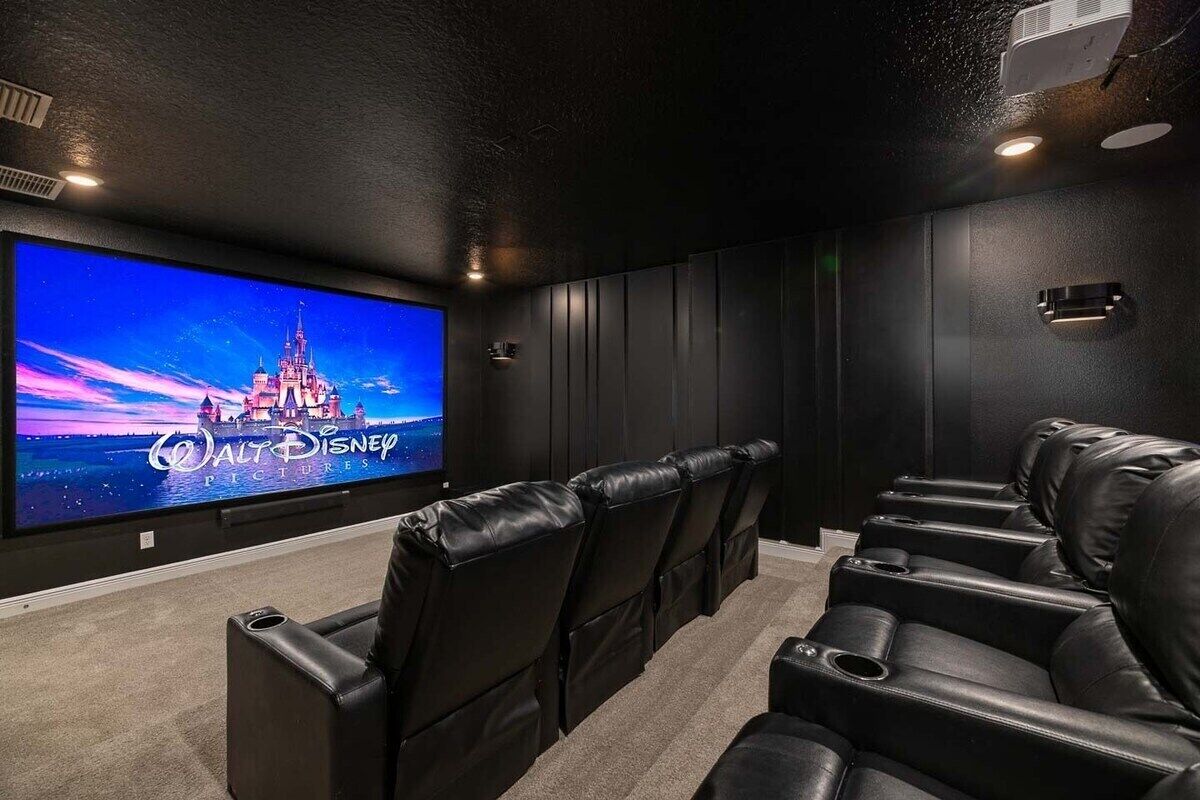 Een bioscoopzaal met een grote flatscreen televisie, zwarte lederen loungestoelen en een vloerbedekking.