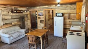 A compact living space with a wooden interior, a sofa, a dining table with chairs, a refrigerator, a microwave, and a stove.