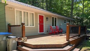 Una cabaña pequeña con una terraza de madera, una puerta roja y dos sillas Adirondack.