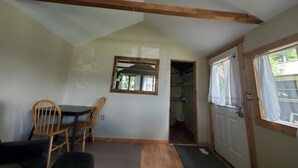 A room with a sloped ceiling, a wooden door, a window with curtains, a mirror, a table with chairs, and a carpeted floor.
