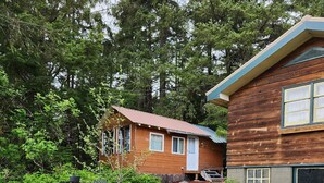 A two-story wooden house with a red roof, a front porch, and a small garden area with a table and chairs.