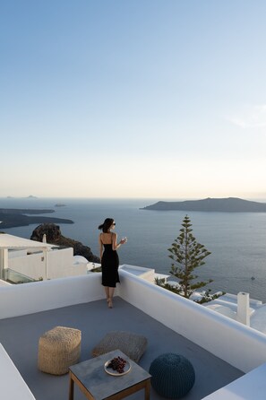 A woman on a rooftop terrace overlooking the sea, with a view of the coastline and a small island.