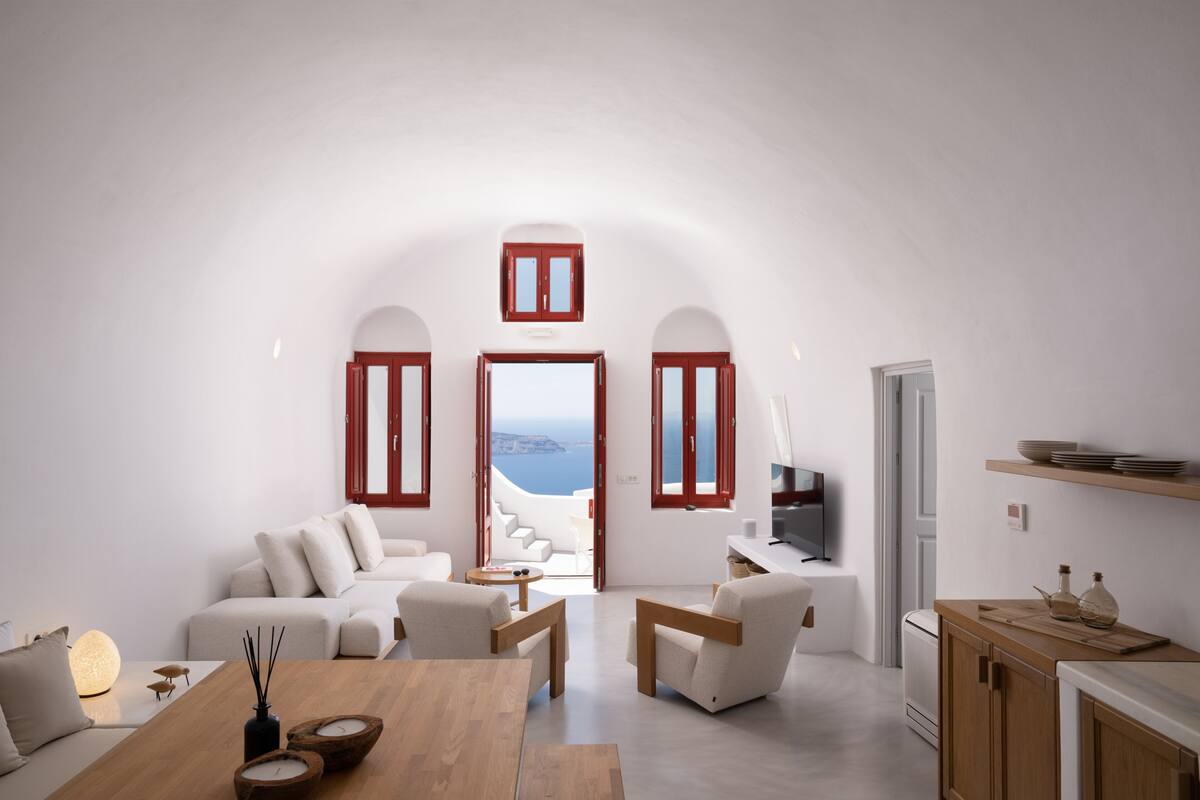 A modern living room with a view of the sea, white walls, and wooden furniture.