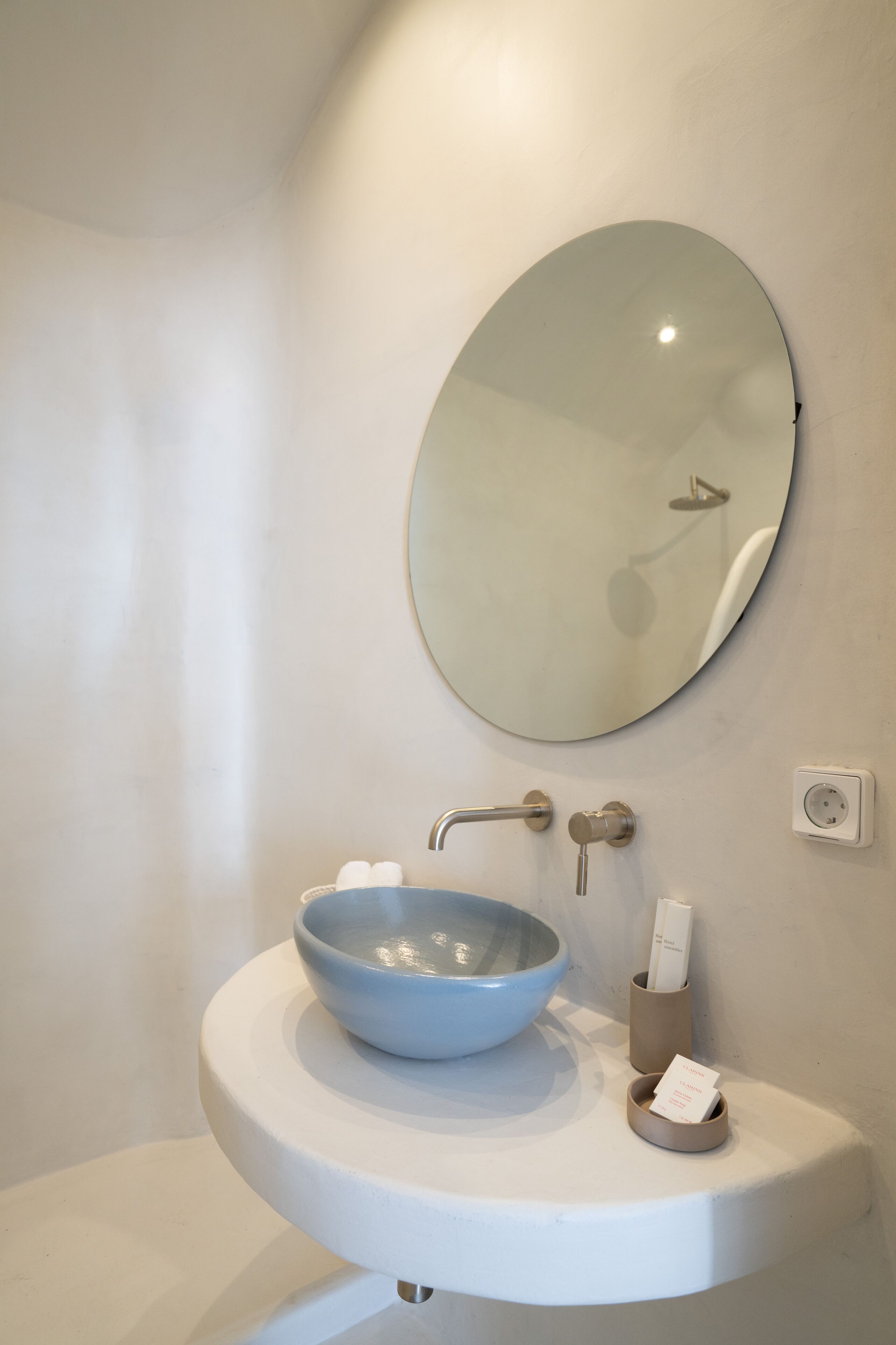 Une salle de bain avec un lavabo blanc, un miroir rond et un distributeur de serviettes.