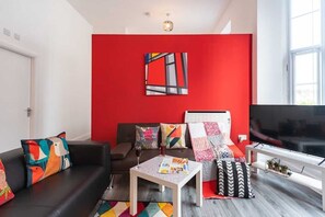 A modern living room with a red accent wall, a black sofa, a white coffee table, and a flat-screen TV. - Modern City Centre Apt Near Theatre & Marina (Kingston upon Hull)