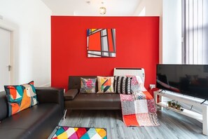 Una sala de estar moderna con una pared de acento roja, un sofá de cuero negro, cojines coloridos, un televisor de pantalla plana y una alfombra estampada.