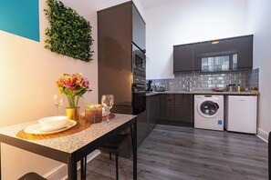A compact kitchen with modern appliances, a dining area with a table set for two, and a built-in washing machine. - Modern City Centre Apt Near Theatre & Marina (Kingston upon Hull)