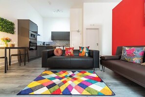 Una sala de estar moderna con un sofá de cuero negro, almohadones coloridos y una alfombra geométrica llamativa.