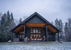 Une cabane avec une cheminée, une terrasse en bois et un porche couvert.