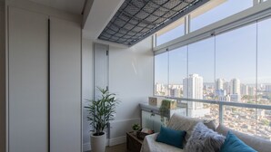 Un salon moderne avec vue sur la ville, un canapé avec des coussins bleus, une plante en pot et une petite table avec des livres et une plante.