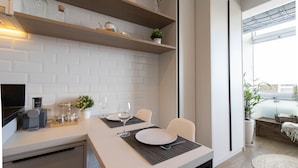 Une cuisine moderne avec des carreaux de céramique blancs disposés en motif métro, des étagères en bois et un coin repas avec une table dressée pour deux personnes.