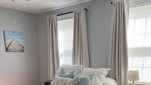 Une chambre à coucher avec un lit, une table de chevet, une lampe et une fenêtre avec des rideaux.