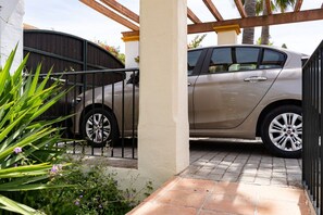 Un auto estacionado en un camino de entrada cubierto, con una verja metálica y un sendero de hormigón.